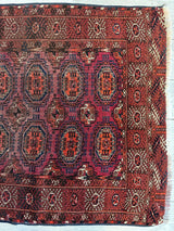 Rectangular antique Turkoman rug with complex geometric motifs in red, brown, and purple hues, framed by multiple patterned borders and fringed edges.