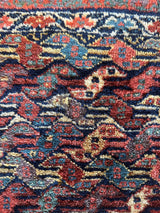 Close-up of a small Kurdish rug section with a repeating serpentine pattern in red, blue, cream, and navy colors on a textured woven background.