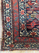 Corner of a small Kurdish rug featuring antique natural dyes with red, navy, cream, and blue floral and geometric border patterns on a textured wool surface.