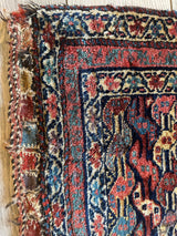 Corner of a small Kurdish rug with antique natural dyes in red, blue, and beige, featuring intricate floral and geometric patterns and frayed edges.