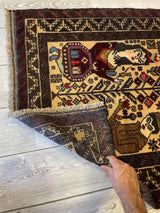 Corner of an antique Afghani Baluchi Laili Majnun pictorial rug showing a woman figure in traditional attire with geometric and floral patterns in dark red, brown, and cream tones.