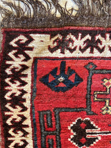 Close-up of an antique tribal bagface with red background, black geometric patterns, ivory and brown border designs, and fringe at the top edge.