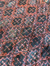Close-up of antique Baluch tribal bag face featuring red, black, and blue geometric diamond patterns with intricate woven details and textured fabric.