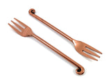 Two copper-finished appetizer forks with a three-prong head and a curled decorative handle end on a white background.