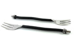 Two cocktail forks with twisted black handles and shiny three-pronged silver metal heads, laid on a white background