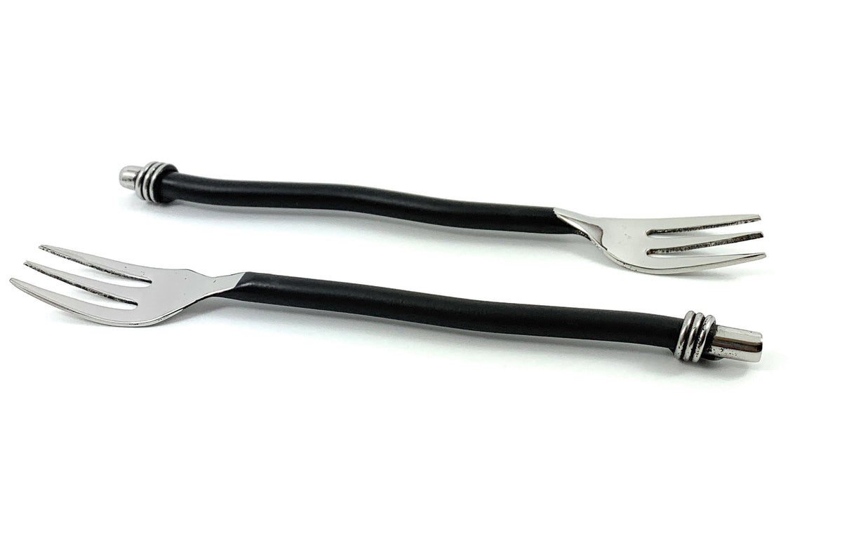 Two cocktail forks with twisted black handles and shiny three-pronged silver metal heads, laid on a white background