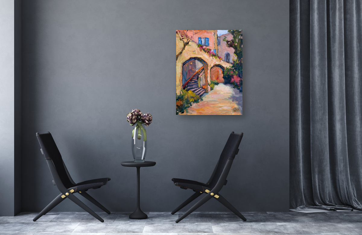 Colorful canvas print depicting sunlit arches and steps in warm pink, orange, and blue tones, hung on a dark gray wall between two black chairs and a small table with flowers.