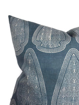 Square pillow with intricate white geometric and floral pattern on lake blue fabric, showing pointed corner and textured weave.