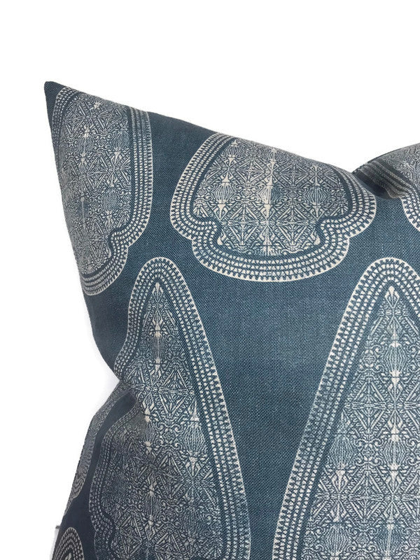 Square pillow with intricate white geometric and floral pattern on lake blue fabric, showing pointed corner and textured weave.