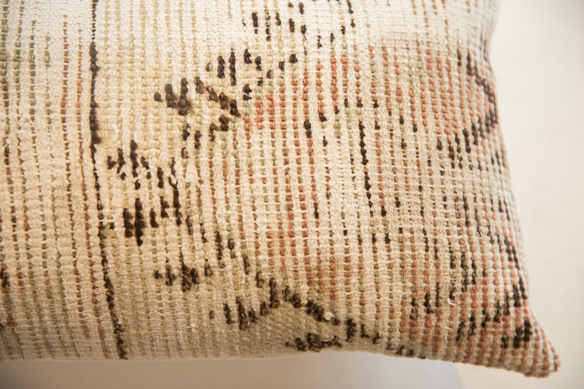 Close-up of a textile pillow with a vintage rug fragment pattern in muted beige, brown, and soft coral tones featuring linear and floral elements.
