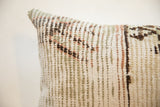 Close-up of a pillow with a vintage rug fragment pattern in muted beige, brown, green, and soft red tones, showing a textured woven fabric surface.