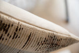 Close-up of a pillow showing textured fabric with beige and brown vintage rug fragment pattern and a light beige plain fabric edge.