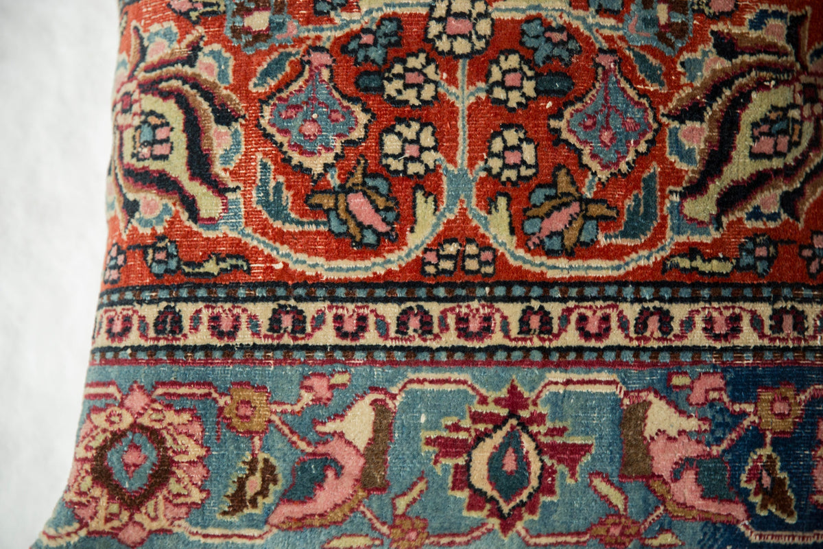 Close-up of a vintage rug fragment pillow featuring intricate floral and geometric patterns in warm reds, blues, and soft pinks with detailed meshed weaving.
