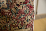 Close-up of a vintage rug fragment pillow showing faded red, beige, blue, and black floral patterns with visible worn threads and texture.