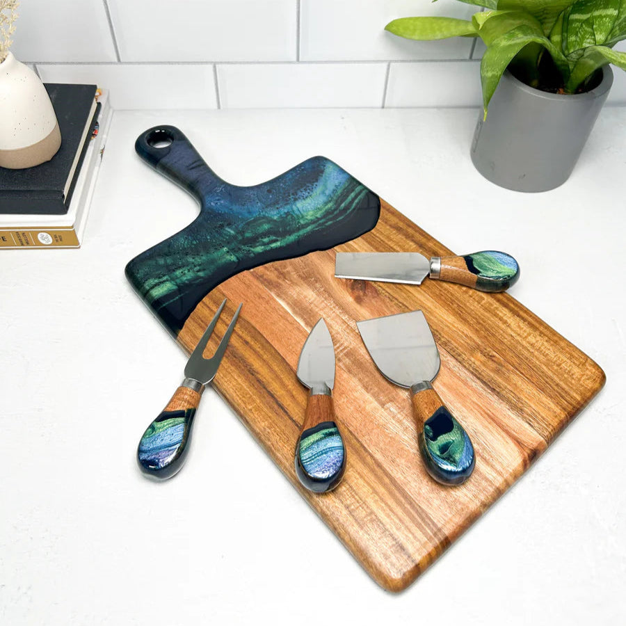 Wooden serving charcuterie board with decorative knives on a white surface with a plant in the background