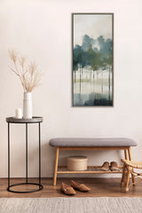 Vertical framed canvas painting of abstract trees in muted greens and blues with misty background, hanging above a wooden bench and side table with dried grasses.