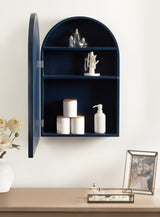Navy blue arched wall cabinet with open door revealing three shelves holding jars, a white pump bottle, a jewelry stand, and silver decor against a beige wall.