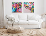 Two vibrant framed canvases above a white sofa, each portrait features colorful flowers and abstract female faces accented in bright pinks, blues, and yellows.
