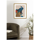 Framed artwork of a vibrant peacock with detailed blue and gold feathers perched among red and dark green peony leaves on a neutral linen background hanging on a white wall above an olive green chair and near a basket with a leafy