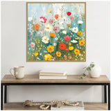 Square canvas painting of colorful wildflowers including yellow, red, white, and pink blooms against a soft blue-green background, framed and hung above a wooden console table.