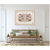 Framed canvas titled 'The Winter Woods' by Vicky Yorke featuring symmetrical brown deer and red berries pattern on cream background, hanging above a wooden bench with green and white pillows.