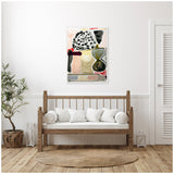 Abstract framed canvas with grey, black, beige, and red shapes hangs above a wooden bench with white cushions in a light minimalist room with a potted plant and round woven rug.