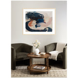 Abstract framed artwork with swirling dark blue, beige, and rust-colored brushstrokes above a pair of dark gray armchairs and a round wooden coffee table with white vase and magazines.