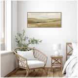 Framed canvas wall art above a wicker armchair with white cushion and wooden side table with textured white lamp, set in a light, minimalist bedroom corner.