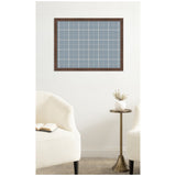 Wall-mounted fabric pinboard with a light blue and white plaid pattern framed in dark wood, above a small brass side table and two cream-colored armchairs.