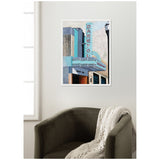 Framed canvas print of a vintage theater marquee reading 'DARE YOU' with Art Deco architectural details in teal and beige colors, hung on a light-colored wall above a dark olive chair with a knit throw.