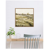 Framed square canvas print of a serene green and beige field landscape with trees and soft brushstrokes, hanging above a minimalist wood desk with a plant and decorative wire sphere.