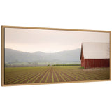 Red barn with a white roof on the right, adjacent to a field with neat rows of young crops stretching toward distant gray-green hills under a soft pastel sky.