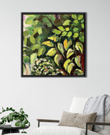 Framed 30x30 canvas painting by Sylvie Blank depicting lush green and yellow leafy foliage with expressive brushstrokes, hung above a white armchair with a beige cushion and gray throw.