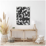 Black and white floral canvas artwork with scattered daisy-like flowers framed and hung above a rustic wooden console table in a neutral, natural-toned room.