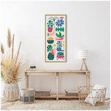Tall narrow framed canvas displaying retro-style, brightly colored abstract floral and succulent shapes in pink, green, blue, and yellow, hanging above rustic wooden console table.