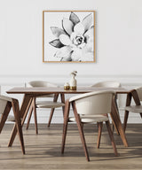 Black and white close-up of a succulent flower with broad petals on a square canvas with a light wood frame hung on a white wall above a modern dining table.