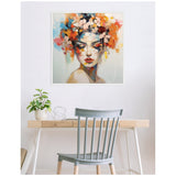 Framed colorful abstract painting of a female figure with vibrant flowers in her hair, hung above a minimalist wooden desk and gray chair in a bright room.