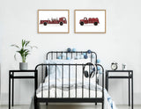 Black metal bed with white bedding under two framed vintage red toy fire truck prints, flanked by black bedside tables holding a plant and an alarm clock