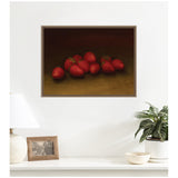 Framed still life painting of ripe red strawberries on a dark brown background, hanging above a white console with lamp, photo frame, and potted plant.