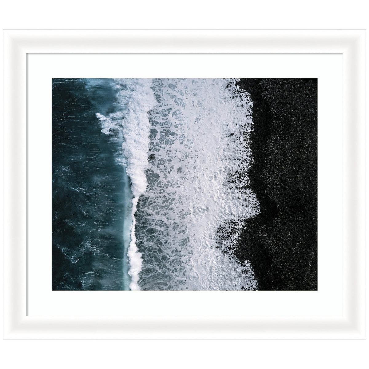 Aerial view of dark ocean waves crashing onto a black pebble beach, with white foam creating textured patterns along the shoreline.