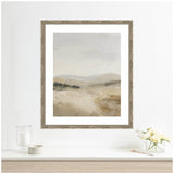 Framed abstract landscape painting with soft beige and gray tones depicting misty fields and hills under a cloudy sky, hanging above a white shelf with glass and flowers.