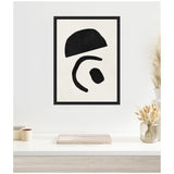 Black geometric shapes including a semicircle, curved line, and circle arranged on a white canvas in a thin black frame hung above a white countertop with neutral decor.