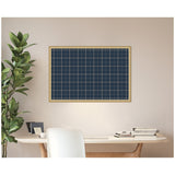 Rectangular wall pinboard with navy blue plaid fabric framed in light wood, mounted above a white desk with books and a plant beside it.