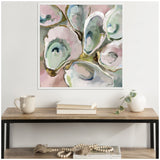 Abstract painting of overlapping oyster shells in soft greens, blues, and pinks with gold-toned outlines, framed and hung above a wooden shelf with books, mug, and ceramic vase.