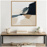 Abstract coastal landscape painting with bold black and blue cliffs, beige sand, and white sea foam, framed and hung above a wooden console with a mug, books, and vase.
