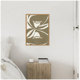 Abstract botanical canvas with large white cutout flower shapes on a muted olive green background, framed in light natural wood and hung above a rustic wooden side table.
