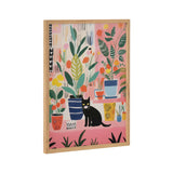 Framed print featuring a black cat surrounded by colorful potted houseplants on a pink background with abstract patterns.