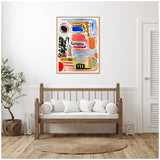 Abstract painting with bold shapes and colors including pink, blue, black, and orange on a white canvas, framed and hung above a wooden bench with white cushions.