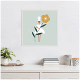 Minimalist illustration of a woman in a white dress holding a large yellow flower with green leaves on a light blue background, framed and hung on a white wall above a desk.