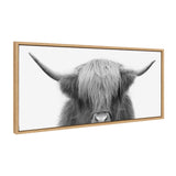 Black and white close-up of a Highland cow with long shaggy hair covering its eyes and long curved horns, framed in light wood.